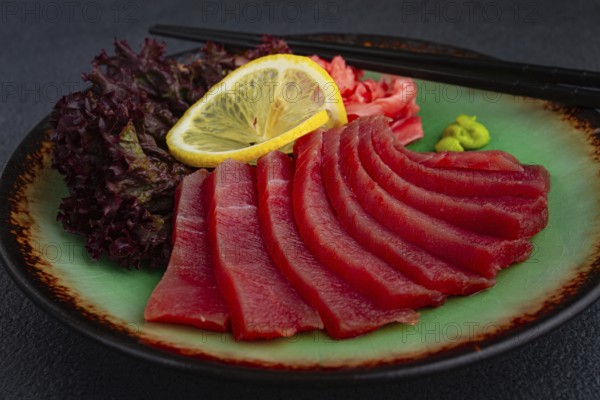 Fresh tuna sashimi served with lemon, wasabi, and pickled ginger on a dark background