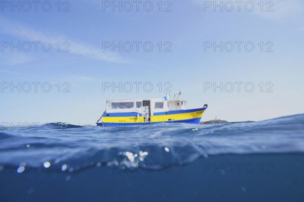 A yellow-blue boat, motor ship, dive boat floats on the calm sea under a clear sky on the Mediterranean Sea near Hyères, Giens peninsula diving site, Porquerolles, Provence, Côte d'Azur, France