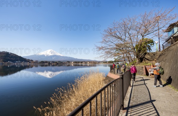Tourists take pictures on the waterfront, Volcano Mt. Fuji is reflected in Lake Kawaguchi, Yamanashi Prefecture, Japan