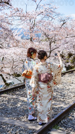Keage Incline, two Japanese women wearing kimonos taking selfies on old tracks, cherry trees blooming on disused tracks, Hanami, cherry blossoms in spring, Kyoto, Japan