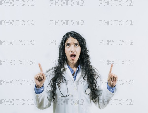 Young female doctor looking and pointing promotion up isolated. Surprised female doctor pointing up
