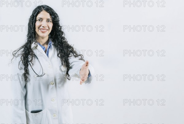 Latin female doctor shaking hands at the camera gesturing welcome. Smiling female doctor gesturing welcome, isolated