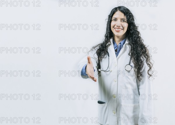 Smiling female doctor gesturing welcome, isolated. Latin female doctor shaking hands at the camera gesturing welcome