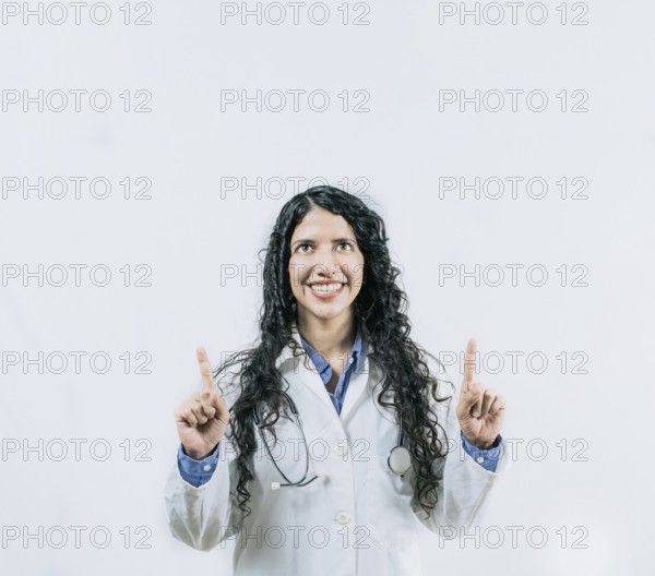 Cheerful female doctor pointing up isolated. Young female doctor looking and pointing at promotion up isolated