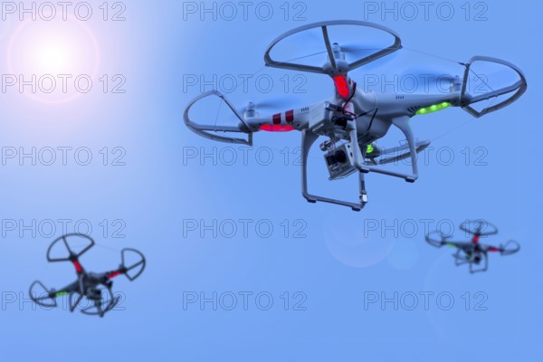 Three miniature quadcopter drones, teleoperated unmanned aerial vehicles, UAV equipped with cameras for aerial photography in flight in group. Digital composite. Sun digitally added