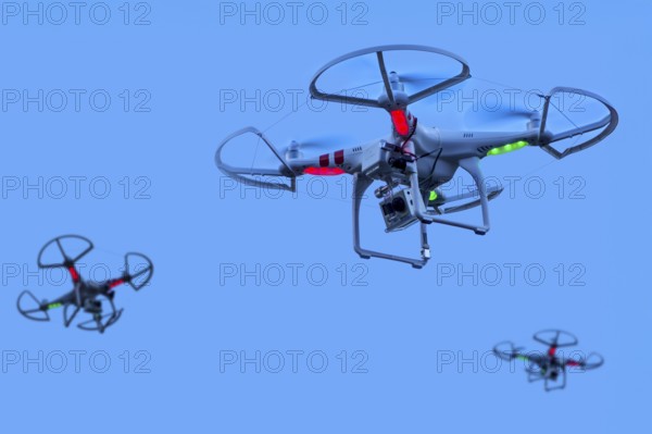 Three miniature quadcopter drones, teleoperated unmanned aerial vehicles, UAV equipped with cameras for aerial photography in flight in group. Digital composite