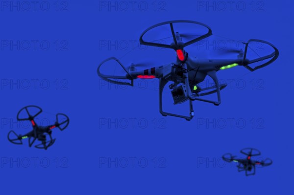 Three illuminated miniature quadcopter drones, teleoperated unmanned aerial vehicles, UAV equipped with cameras for aerial photography in flight at night. Digital composite