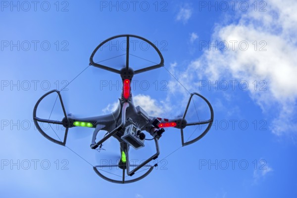 Miniature quadcopter drone, teleoperated unmanned aerial vehicle, UAV equipped with camera for aerial photography in flight against blue sky