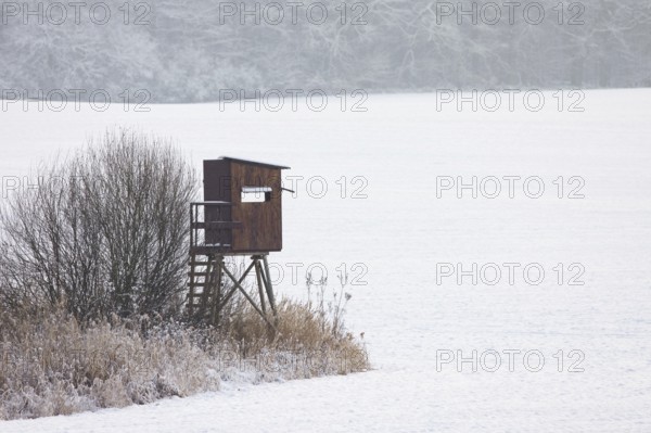 Raised hide, hunting blind, deerstand, deer stand in snow covered field at edge of forest in winter