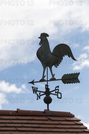 A dark weather vane on a roof against a blue sky with clouds, Baden-Württemberg, Germany