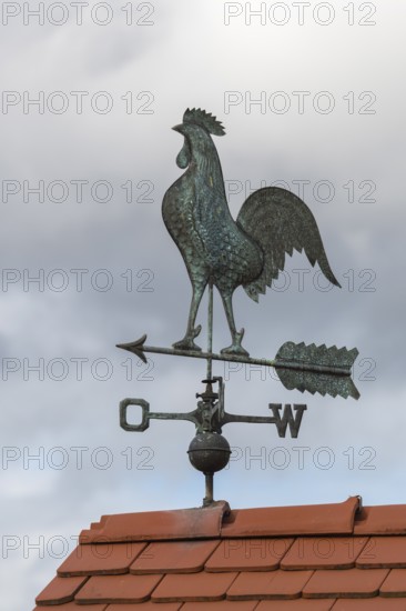 Metal weather vane with rooster on a tiled roof against cloudy sky, Baden-Württemberg, Germany