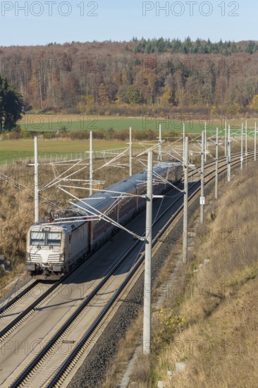 A passenger train travels on a railway line through an autumnal landscape with fields and forests, surrounded by overhead lines, new Stuttgart-Munich line, near Dornstadt, Swabian Jura, Baden-Württemberg, Germany