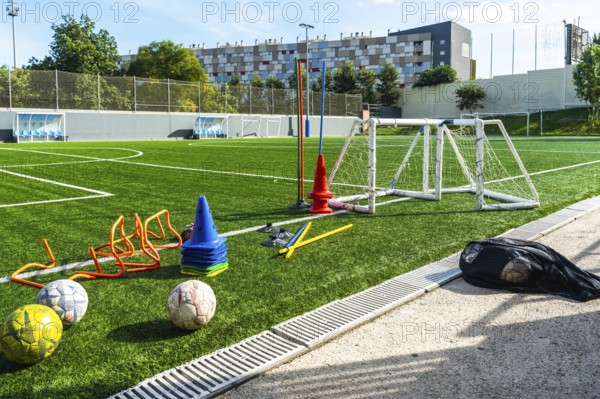 Artificial grass soccer field with multiple training equipment including cones, hurdles, a small goal, and soccer balls, ready for practice exercises under sunlight