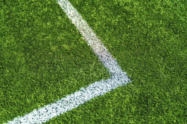 Green artificial turf creating a textured background with a white painted line marking a corner of a sports field, symbolizing boundaries, precision, and athletic competition