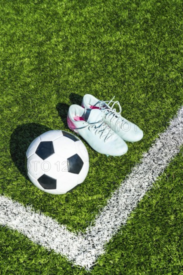 Soccer ball on artificial green turf beside light blue cleats and white boundary line, close top view evoking training, competition, preparation and active outdoor play