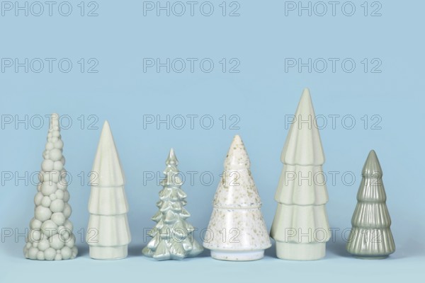 Row of different shaped light green ceramic Christmas trees on blue background