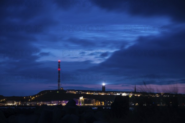 Panoramic view, view of the highlands of the island of Heligoland at night with red-lit radio tower, radio tower, transmitter, bright lighthouse, dark church tower and deep blue sky with lots of clouds above, nighttime lowland in front of it, rest of sunset in the night sky, quiet and dark atmosphere, cloud bank, weather, summer, night shot, long exposure, beacon, maritime, North Sea, Pinneberg district, Schleswig-Holstein, Germany