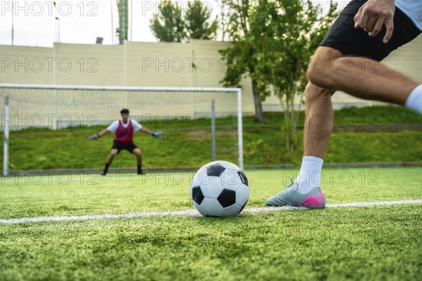 Football player preparing to shoot a penalty kick with the ball on the artificial turf, facing a focused goalkeeper standing in the goal, creating an intense moment of athletic competition