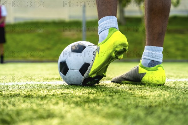 Soccer player foot in neon green cleats controlling a black and white ball on synthetic turf in daylight, low angle close up conveying focus, readiness and athletic action