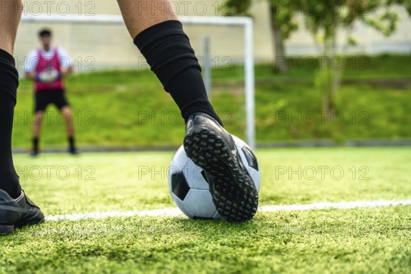 Soccer players foot about to strike the ball for a penalty, blurred goalkeeper in background on green artificial turf during a tense match, focused action shot