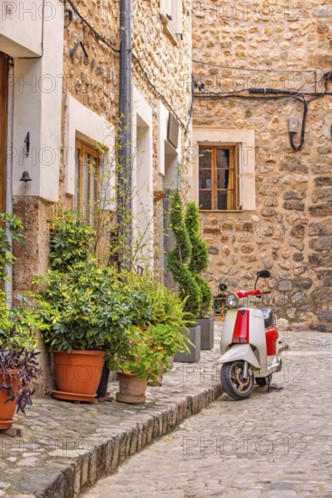 Scooter parked on a street in an idyllic city street with green plants in front of the houses on the sidewalk, Soller, Mallorca, Spain