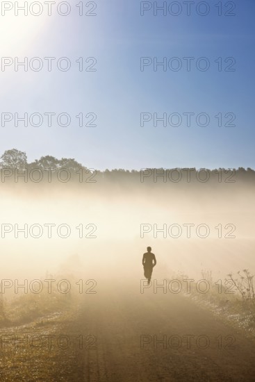 Man running on a dirt road in fog and morning sunshine in the countryside