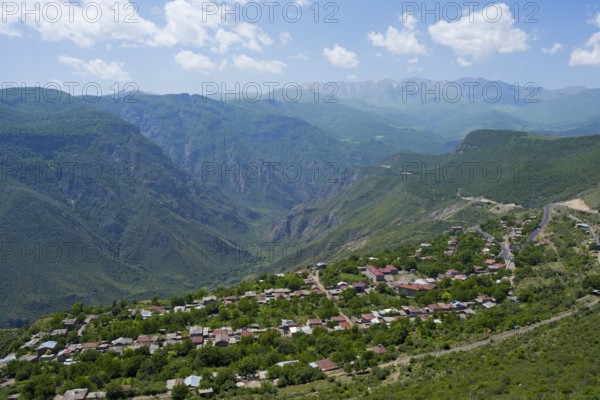 A small village is situated in a green valley surrounded by forested mountains under a cloudy sky, Halidzor, view from Wings of Tatev, Syunik province, Caucasus, Armenia