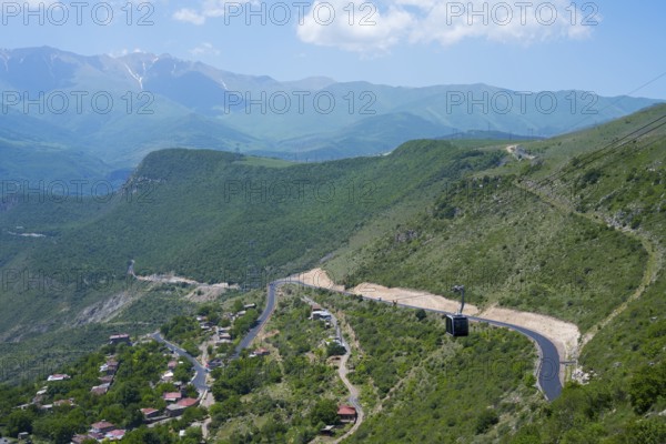 A winding road runs through green hills and passes a small village, with views of mountains, Tatev cable car, Wings of Tatev, Wings of Tatev, Halidzor, Syunik province, Caucasus, Armenia