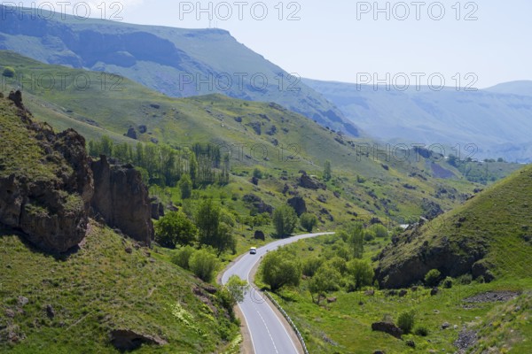 A winding road leads through a green valley with hills and trees under a blue sky, landscape between Aghitu and Vorotnavank Monastery, Vorotnavank, Syunik Province, Caucasus, Armenia