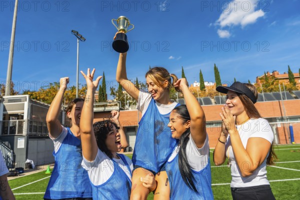 Happy young women soccer players celebrating victory on a sunny outdoor field, lifting the championship trophy together with smiles, teamwork and energetic joy after the win
