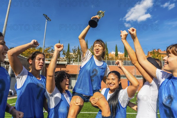 Female athletes sharing joy and success, lifting their teammate holding a trophy after winning a soccer match, representing teamwork and achievement in sports
