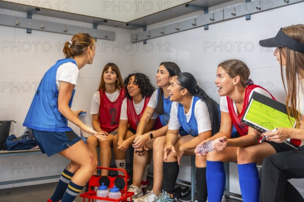 Women's soccer team players are attentively listening to their coach explaining game strategy and a pep talk a in a locker room, focusing on teamwork and preparing for competition