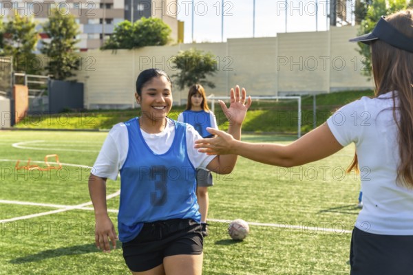 Young female soccer player smiling and high fiving her coach on a green field during practice, symbolizing teamwork, encouragement, and dedication in women's sports