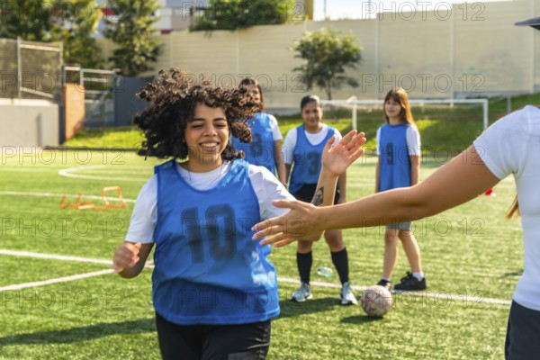 Young female soccer player high fiving her coach on a green artificial turf field, training with her team and celebrating teamwork and success during a sports activity