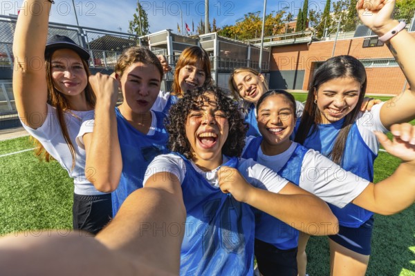 Young diverse women's soccer team playing a championship, celebrating a goal or victory together while taking a selfie on a green turf field, emphasizing teamwork, joy, and success