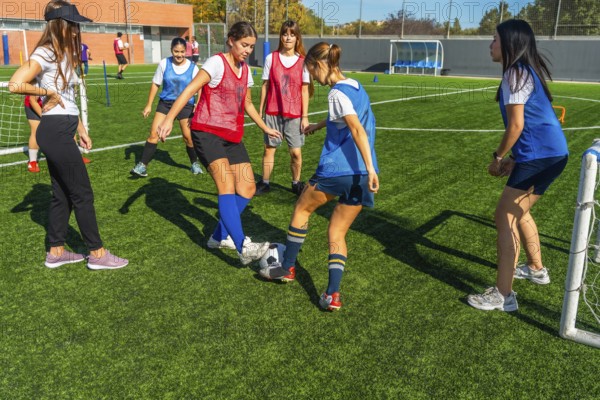Young women soccer players are practicing passing and dribbling drills on a green artificial turf field, developing their skills and teamwork during a sunny day