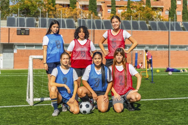 Diverse group of women on a soccer field, some standing and some crouching, wearing jerseys and bibs, confidently posing as a team before a match or training session