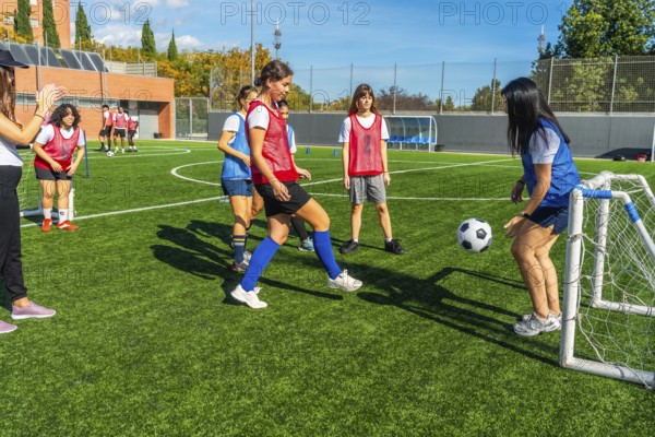 Young females training soccer on an artificial turf field, engaging in a small sided game with a goal, showcasing teamwork and dedication in a vibrant outdoor setting