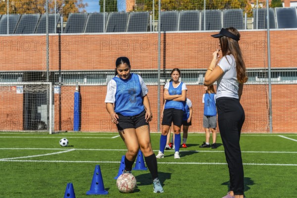 Female soccer players receiving instructions from their coach during a practice session on a green turf field, focusing on individual ball control drills