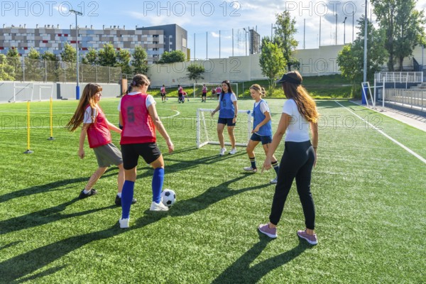 Female soccer teammates training on a sunny artificial turf field, practicing dribbling, passing and teamwork in an energetic outdoor session promoting fitness and youth sport development