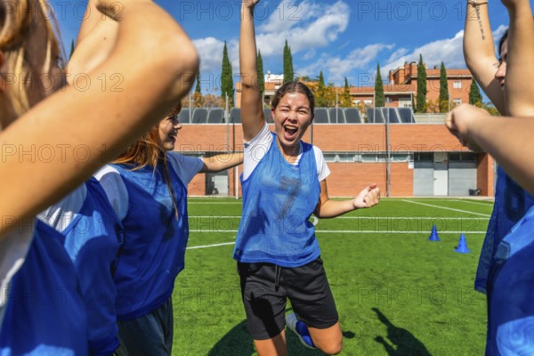 Young women's soccer team celebrating a goal, arms raised and cheering with bright smiles on a sunny field, showing teamwork, victory and joyful energy