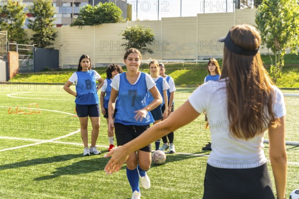 Young women's soccer team participating in a training session on a sunny artificial turf field, receiving instructions from their female coach while practicing their skills and teamwork