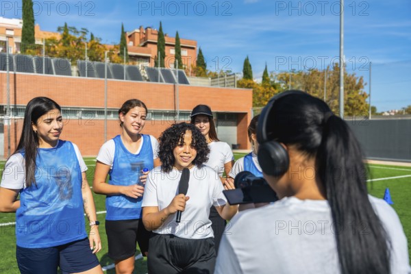 Diverse group of women soccer players being interviewed by a journalist with a microphone and camera on a green football field, highlighting sports media and teamwork