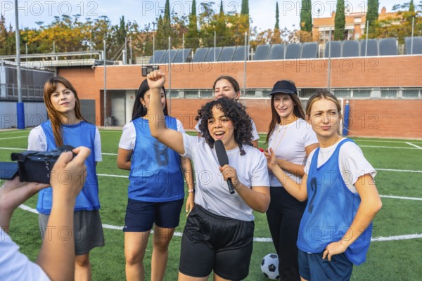 Happy young women's soccer team and coach giving an interview on artificial turf field, celebrating success and empowerment during a group conversation