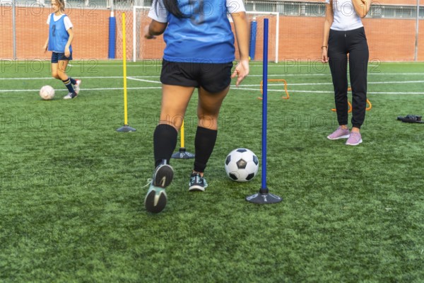 Women athletes practicing soccer on an artificial turf field, dribbling a ball around obstacles during a sports training session, focusing on skill development
