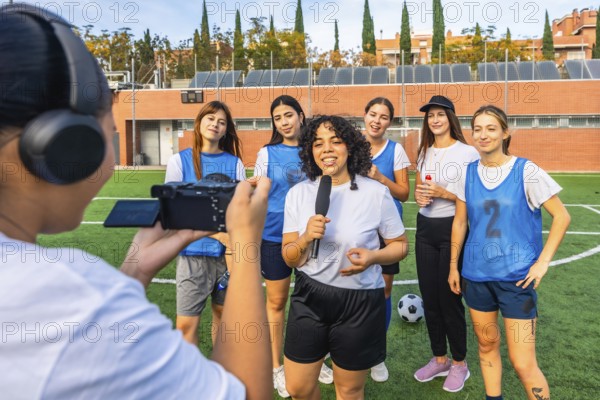 Female sports journalist interviewing a diverse women's soccer team on a green field, capturing their stories and experiences after a training session or game