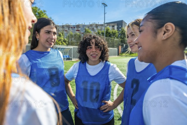 Diverse young women soccer team huddling on a green sports field, collaborating and discussing strategies during outdoor training, focusing on teamwork and friendship