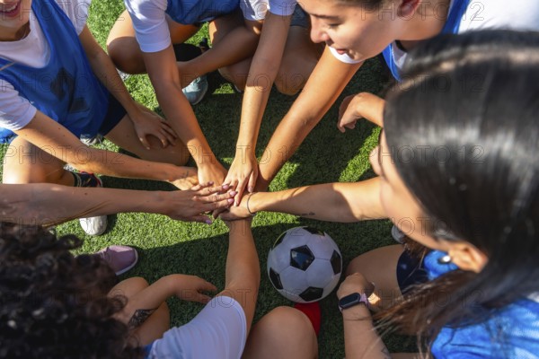 Women soccer players huddling on the green field, joining hands in a sign of unity and strength before an important match, symbolizing friendship, cooperation, and strategic planning