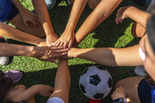 United women soccer players stacking hands in a huddle on the green artificial grass field, showing teamwork, support, and friendship during a practice or match