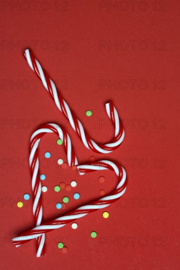 Candy canes and sugar confetti against red background, Christmas